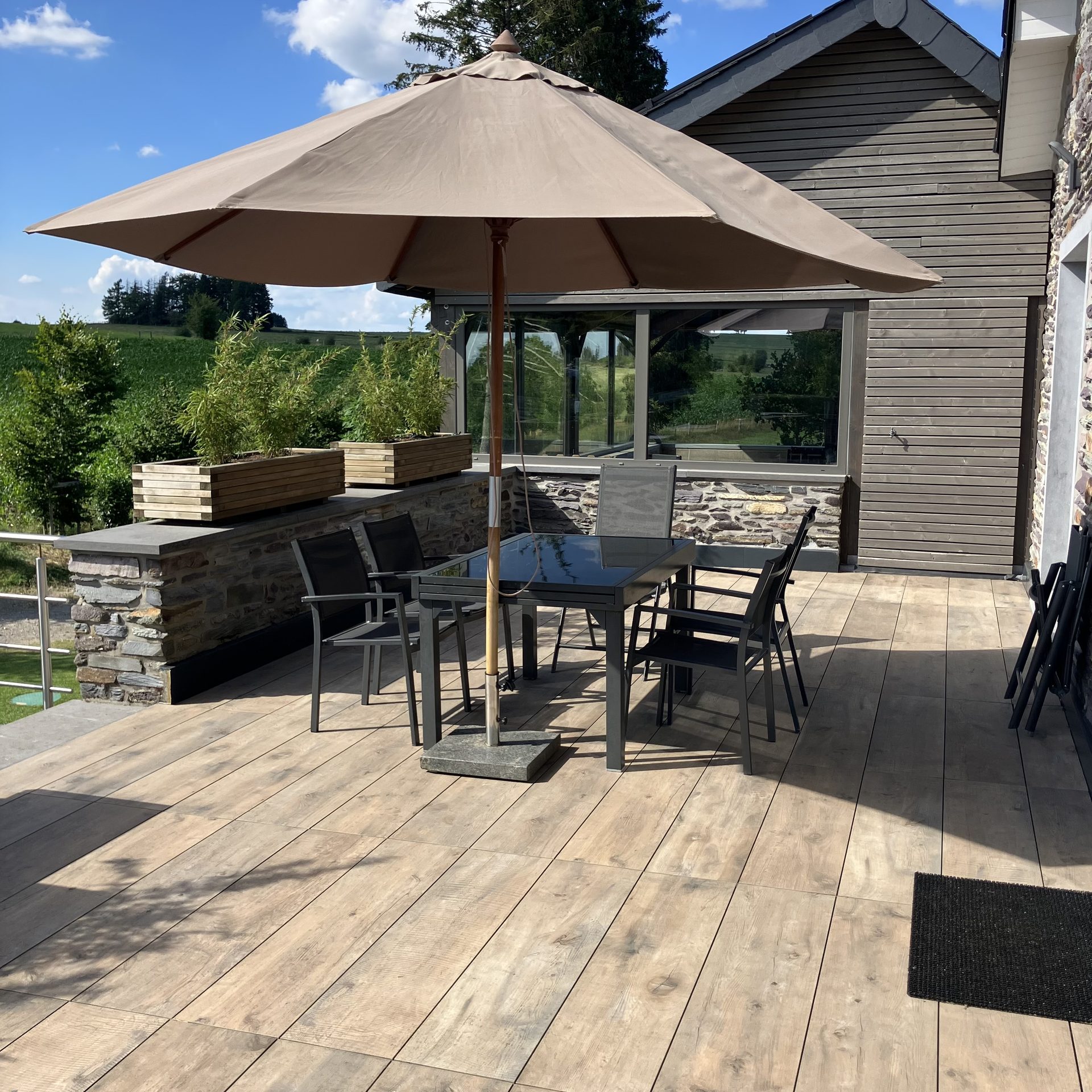 Grande terrasse en bois avec parasol, table et chaises, ouverte sur la campagne