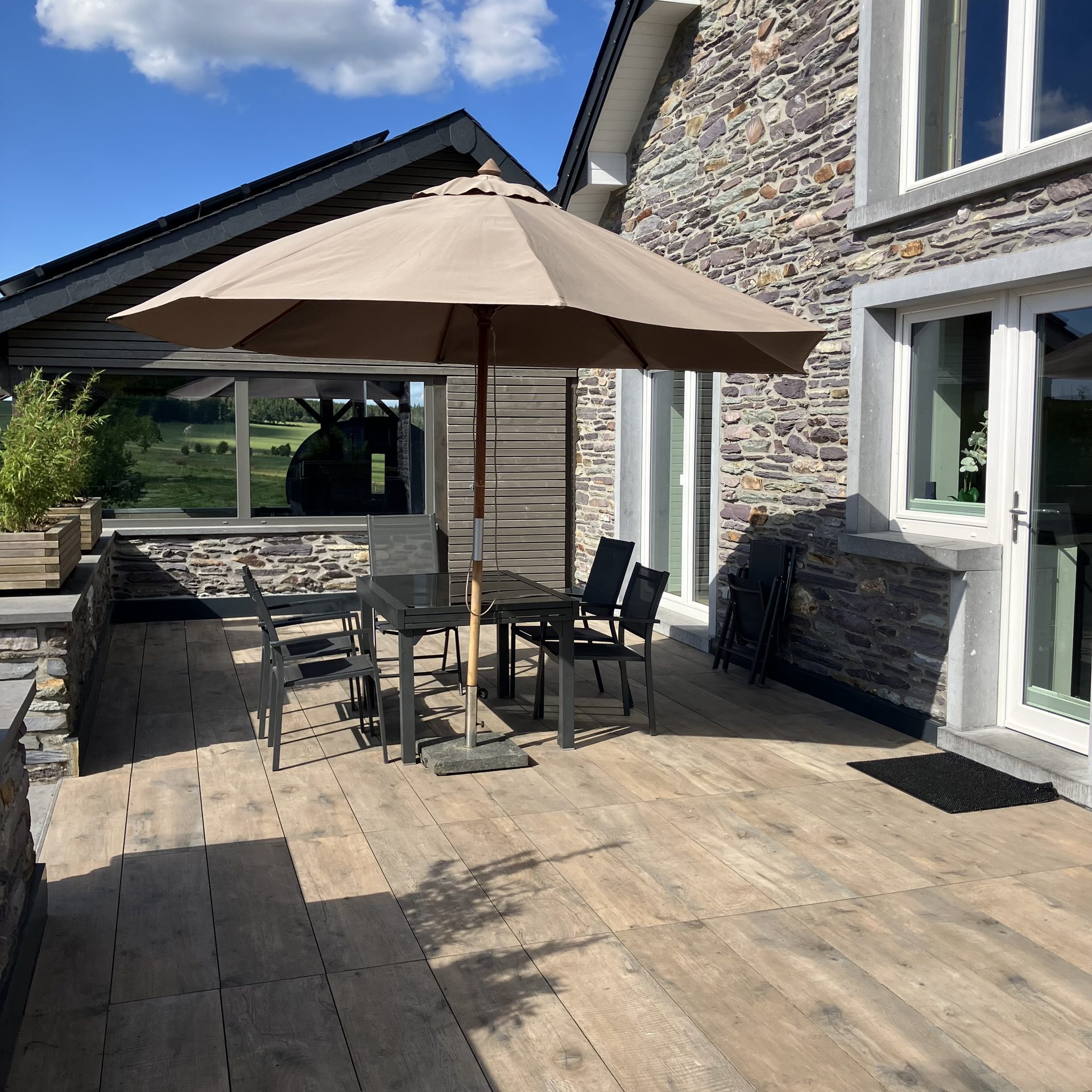 Terrasse ensoleillée le long de la façade en pierre, avec salon de jardin sous parasol